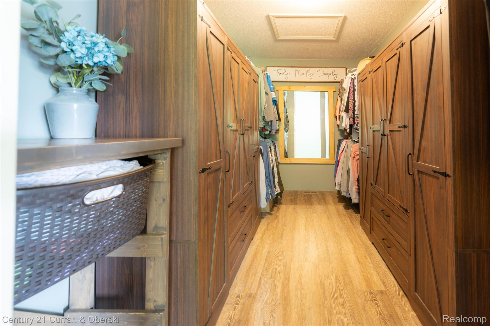 8775 Winding Rdg Drive Millersburg, MI 49759 - Photo 34 of 53 Spacious walk-in closet featuring extensive built-in cabinetry with barn door-style fronts, wood-finish flooring, and a large central mirror