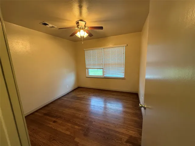 an empty room with wooden floor chandelier fan and windows