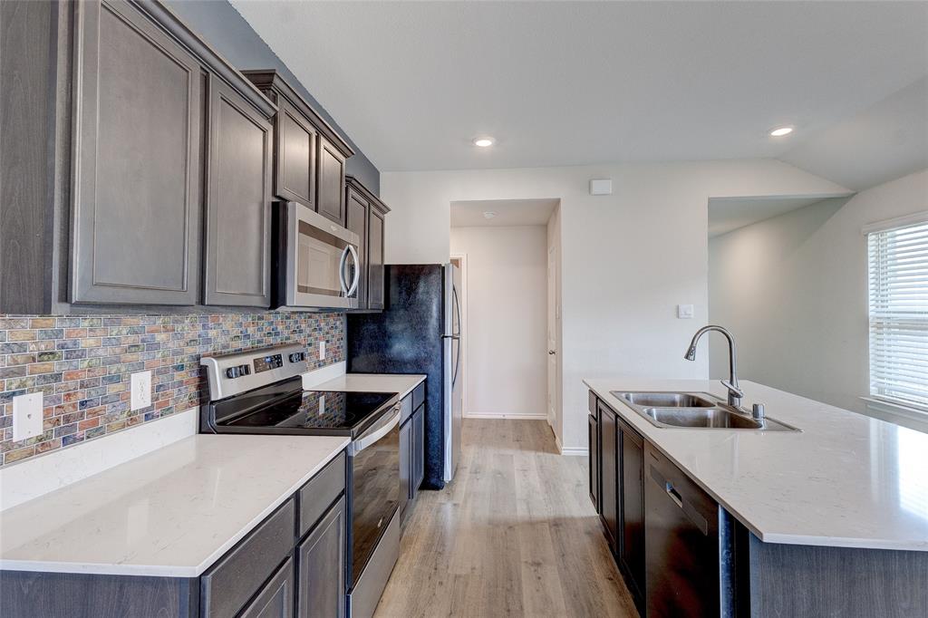 1016 Rio Bravo Drive Forney, TX 75126 - Photo 8 of 25 Modern kitchen featuring dark cabinetry, stainless steel appliances, light countertops, a colorful tile backsplash, and wood-finish flooring