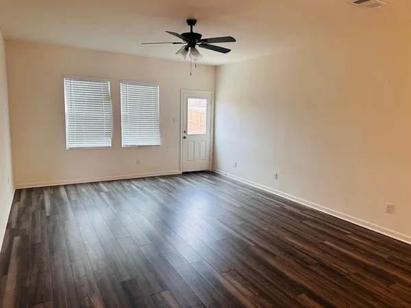 an empty room with wooden floor chandelier fan and windows