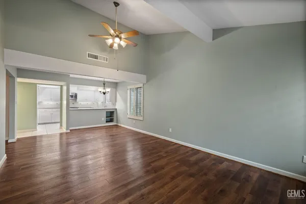 a view of an empty room with wooden floor and a kitchen