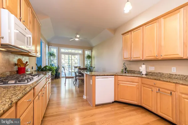 a kitchen with stainless steel appliances granite countertop a refrigerator a sink dishwasher a stove and white cabinets with wooden floor