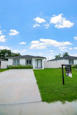 a view of house in front of a big yard with plants and large trees