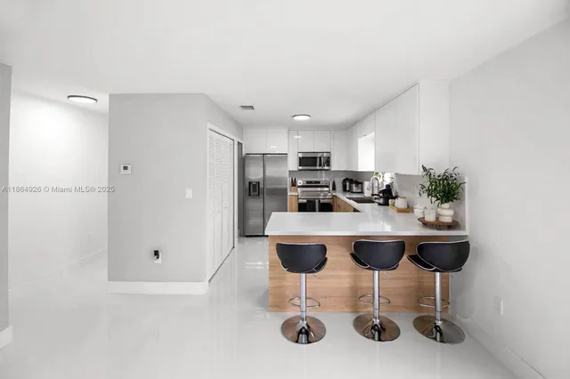 a room with stainless steel appliances kitchen island granite countertop a table chairs a sink and a refrigerator