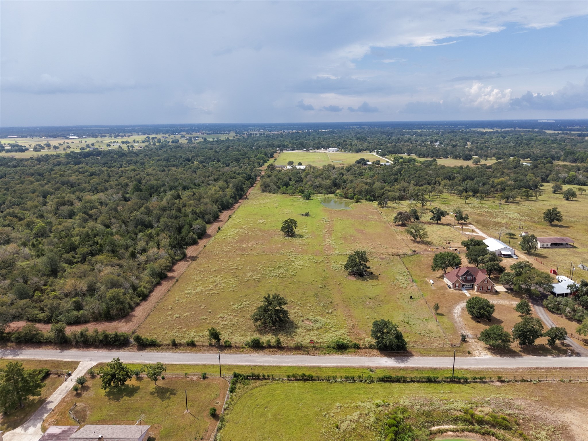 38021 Wiggins Road Hempstead, TX 77445 - Photo 19 of 19 Elevated aerial view showcases the property’s broad road frontage, open pasture, scattered mature trees, and wooded backdrop.