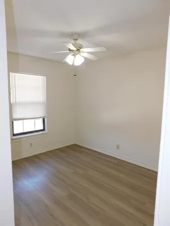 an empty room with wooden floor fan and windows