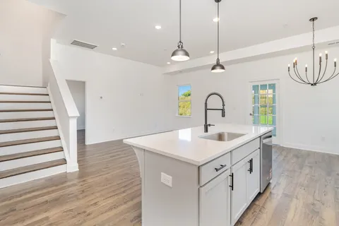 a kitchen with a sink a chandelier stainless steel appliances and wooden floor