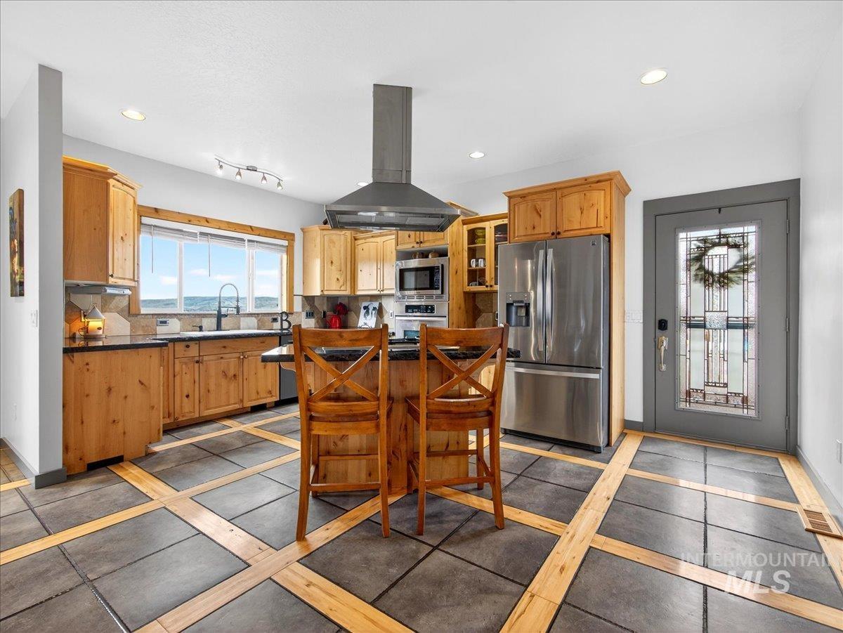 11714 Chukar Ridge Lane Horseshoe Bend, ID 83629 - Photo 18 of 50 Kitchen with island exhaust hood, stainless steel appliances, glass fronted cabinets, dark countertops, and recessed lighting