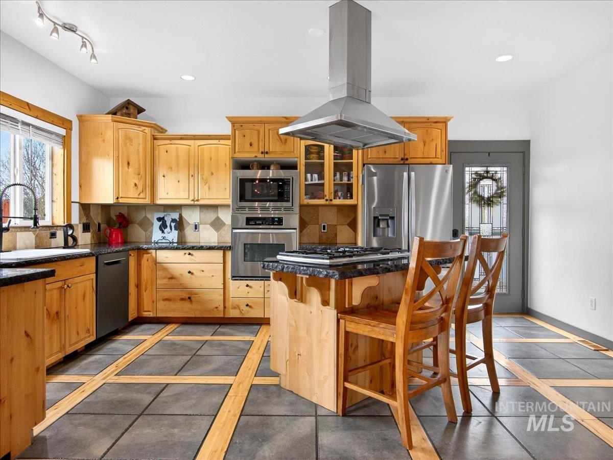 11714 Chukar Ridge Lane Horseshoe Bend, ID 83629 - Photo 19 of 50 Kitchen featuring inlaid floor details, island range hood, a breakfast bar, stainless steel appliances, and backsplash