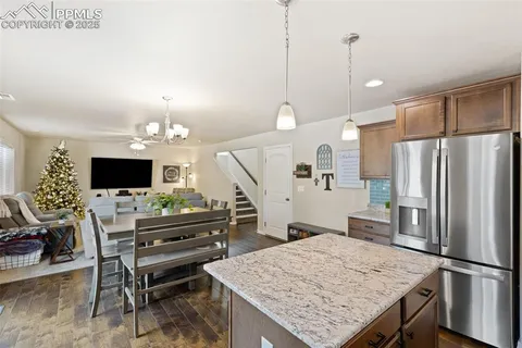 a kitchen with kitchen island a refrigerator a stove a microwave oven a dining table and chairs with wooden floor