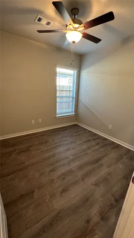 an empty room with wooden floor fan and windows