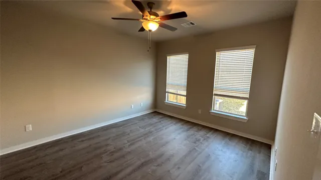 an empty room with wooden floor fan and windows
