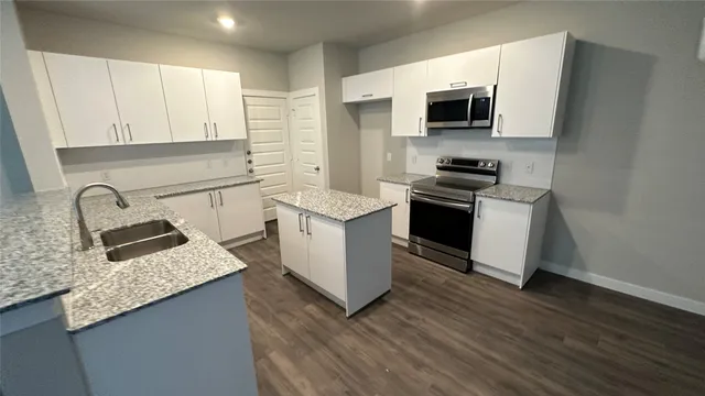 a kitchen with stainless steel appliances granite countertop a stove top oven a sink a refrigerator white cabinets and wooden floor