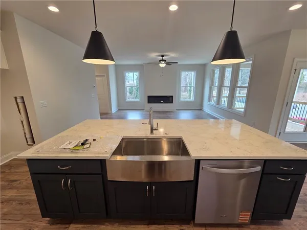 a living room with stainless steel appliances furniture a window wooden floor and a kitchen view
