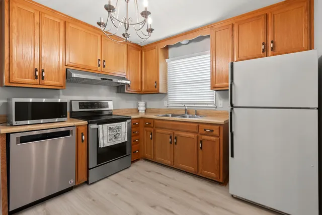 a kitchen with stainless steel appliances granite countertop a refrigerator a sink dishwasher a stove and a dining table with wooden floor