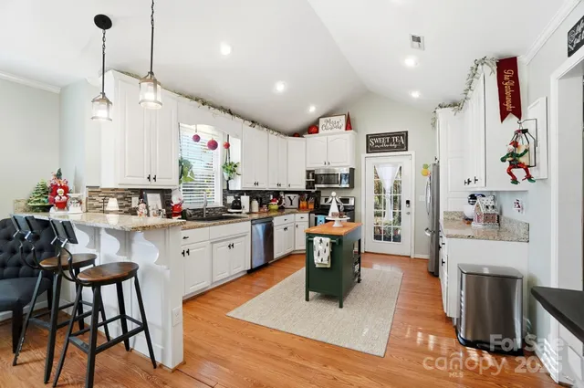 a kitchen with stainless steel appliances kitchen island granite countertop a refrigerator a stove top oven a sink dishwasher and white cabinets with wooden floor