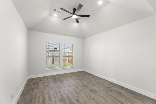 an empty room with wooden floor ceiling fan and windows