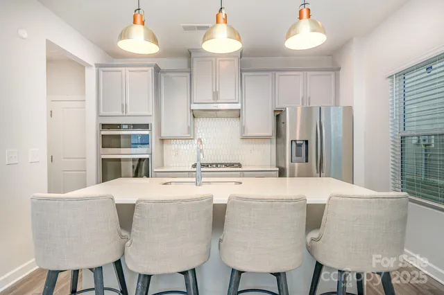 a kitchen with stainless steel appliances a dining table chairs refrigerator and cabinets