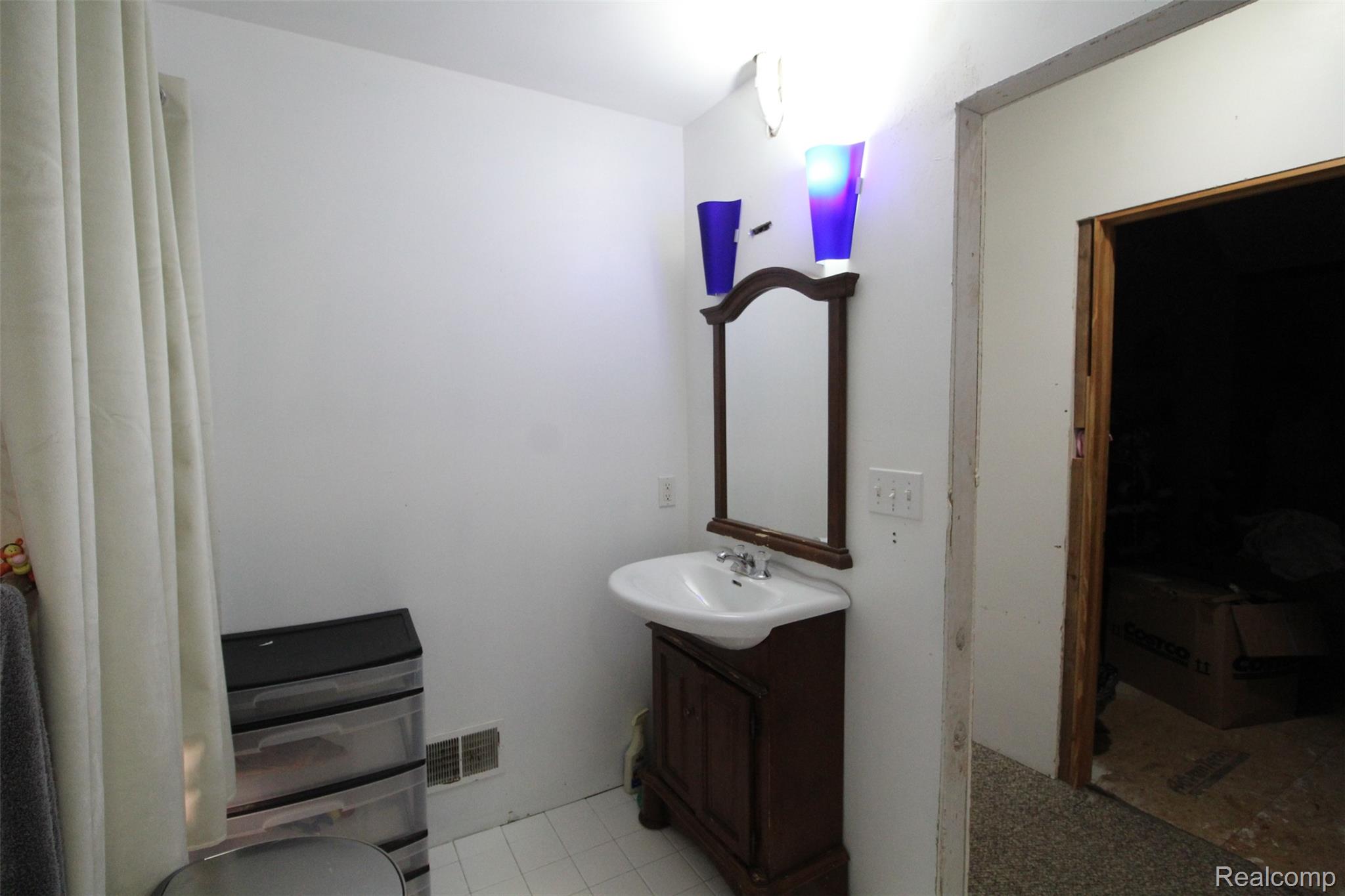 2568 Valentine Road Lapeer, MI 48446 - Photo 24 of 42 Elegant half bath featuring a dark wood vanity with white porcelain sink, framed mirror with decorative sconces, and tile flooring