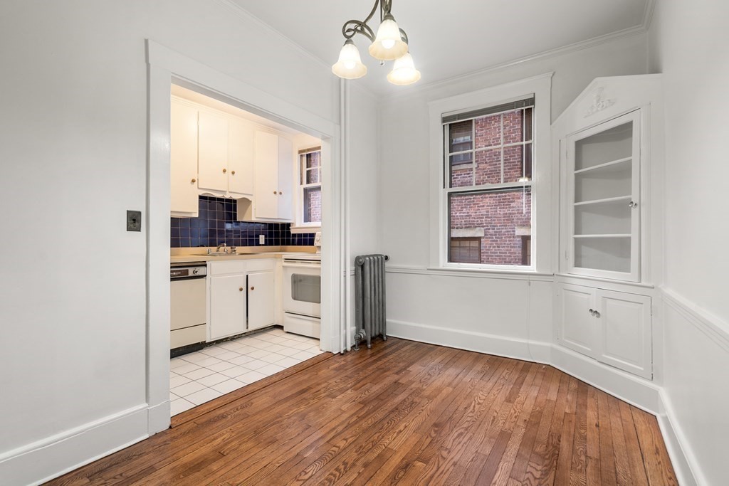135 Freeman Street, Unit 1A Brookline, MA 02446 - Photo 4 of 22 a kitchen with granite countertop a stove a sink and white cabinets with wooden floor next to windows
