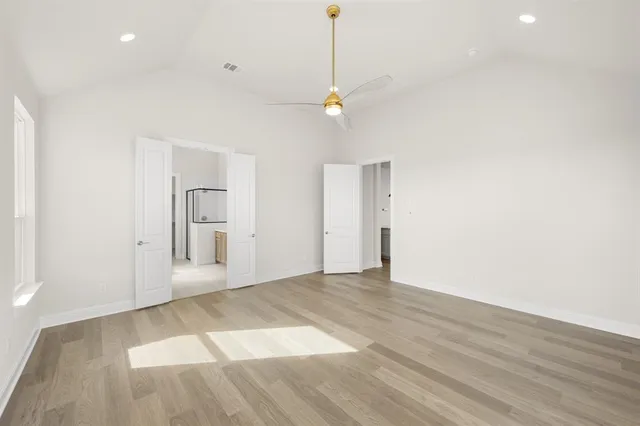 a view of an empty room with wooden floor and a ceiling fan
