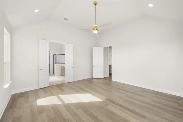 a view of an empty room with wooden floor and a ceiling fan