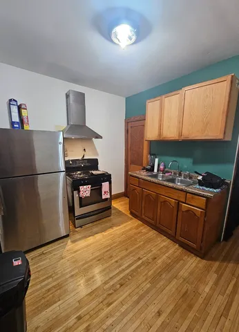 a kitchen with stainless steel appliances kitchen island granite countertop a refrigerator a stove a sink dishwasher and wooden cabinets with wooden floor