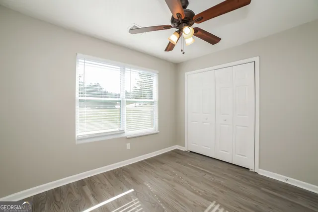 an empty room with wooden floor chandelier fan and windows