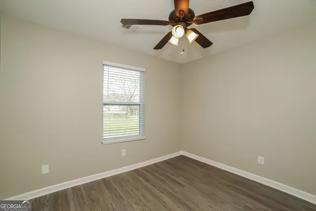 an empty room with wooden floor fan and windows