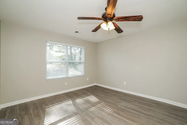 an empty room with wooden floor fan and windows