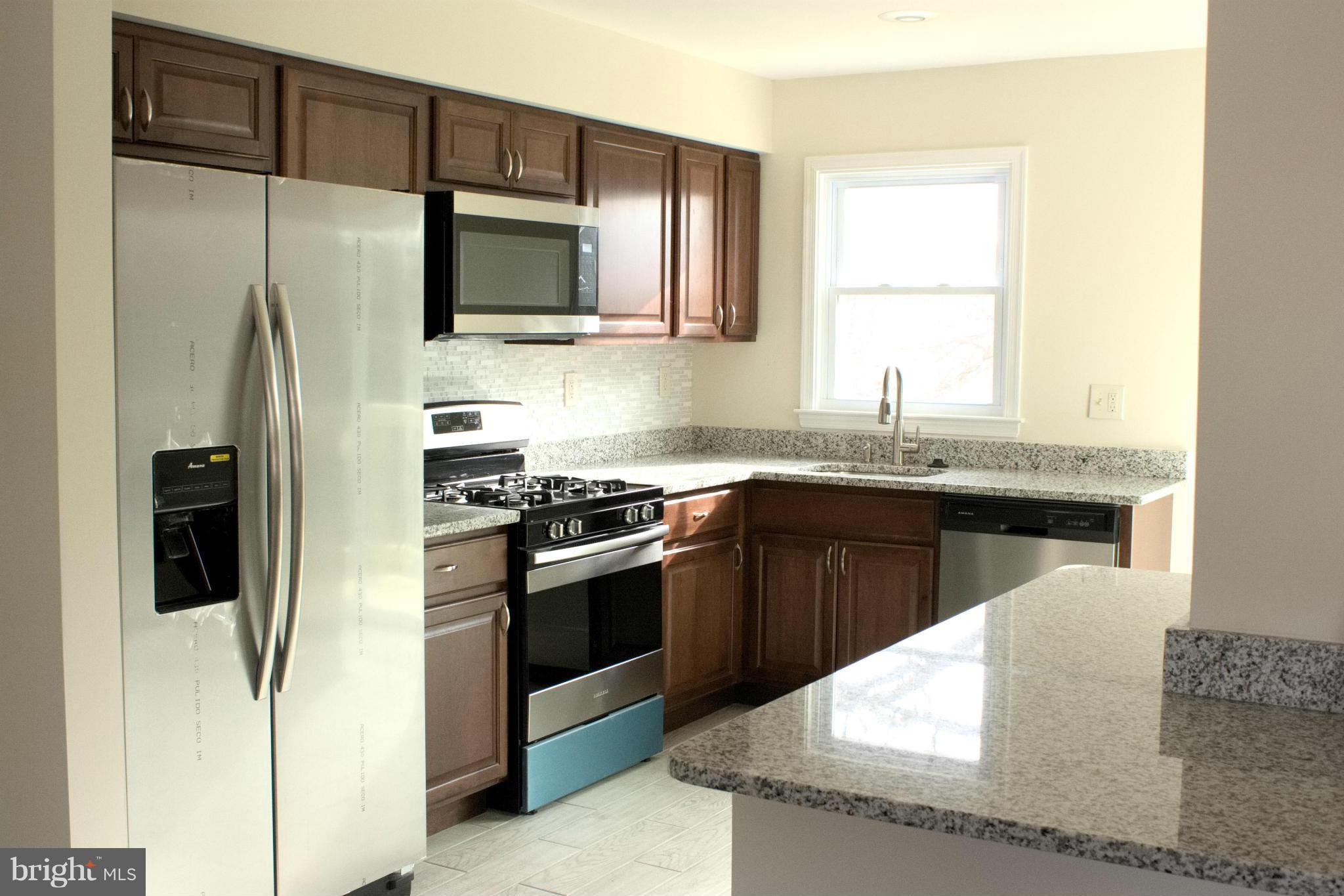 6709 Garvey Road Baltimore, MD 21237 - Photo 5 of 29 a kitchen with stainless steel appliances granite countertop a refrigerator a sink a stove a microwave and wooden cabinets