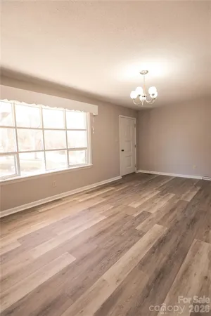 an empty room with wooden floor chandelier and windows