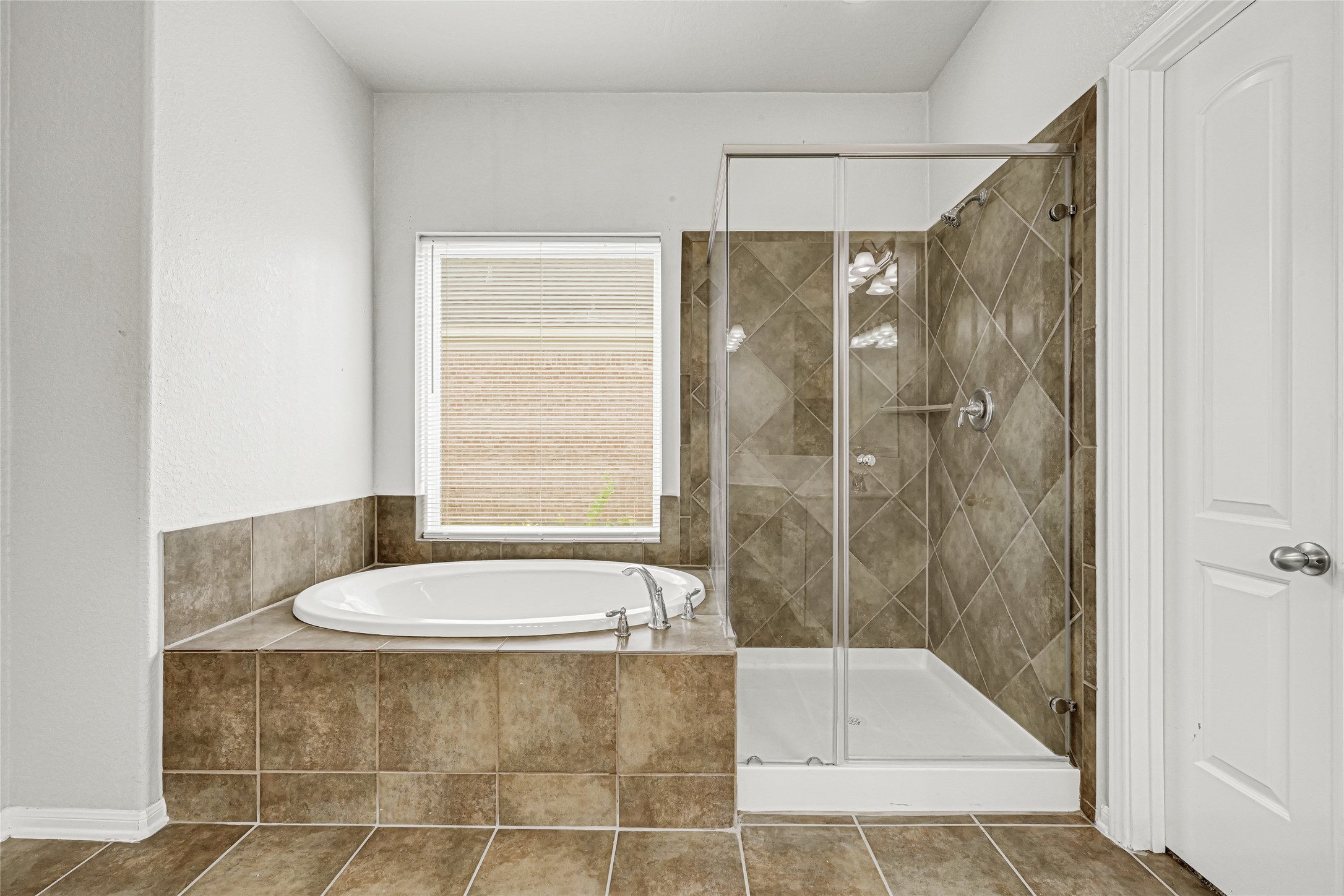 4702 Sedgewood Drive Rosenberg, TX 77471 - Photo 20 of 24 The primary bathroom features a luxurious soaking tub beside a sleek glass-enclosed shower. The neutral tile design adds a modern touch, complemented by a large window providing natural light.