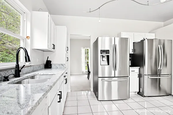 a kitchen with stainless steel appliances kitchen island granite countertop a dining table chairs and a refrigerator