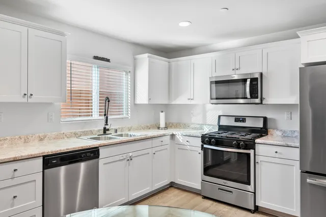 a kitchen with granite countertop white cabinets appliances a sink and a window