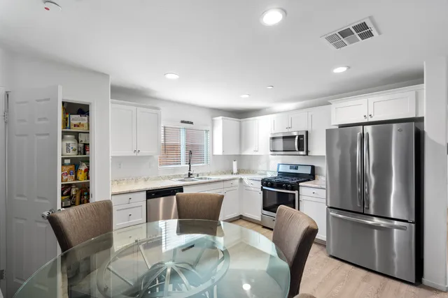 a kitchen with stainless steel appliances a refrigerator a stove a sink dishwasher a dining table and chairs with wooden floor