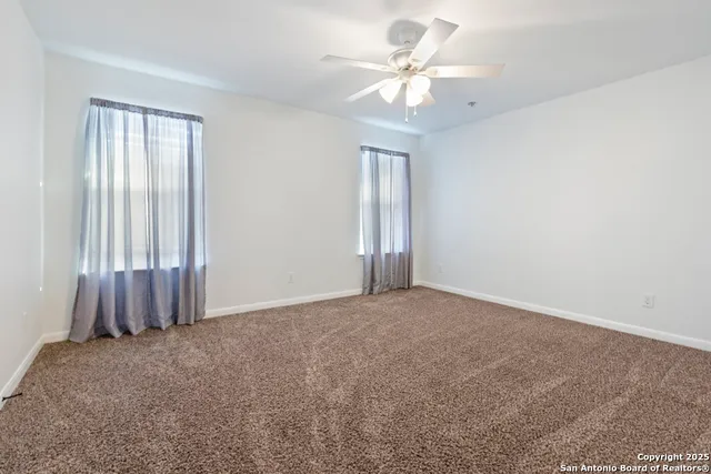 an empty room with a chandelier fan and windows