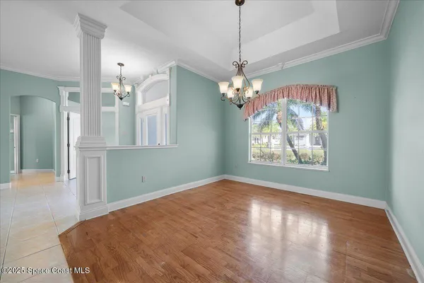an empty room with wooden floor chandelier and windows