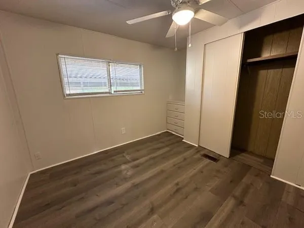 an empty room with wooden floor fan and windows