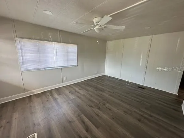 an empty room with wooden floor fan and windows