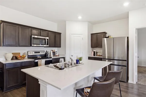 a kitchen with a refrigerator a stove a sink dishwasher a dining table and chairs with wooden floor