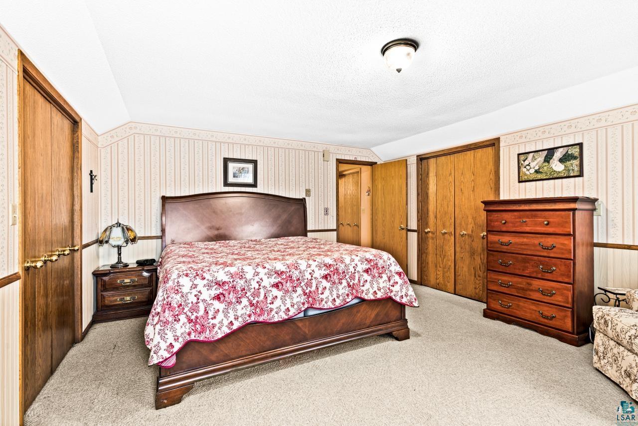 3723 Birchwood Road Kettle River, MN 55757 - Photo 29 of 48 Carpeted bedroom featuring lofted ceiling, wallpapered walls, multiple closets, and a textured ceiling
