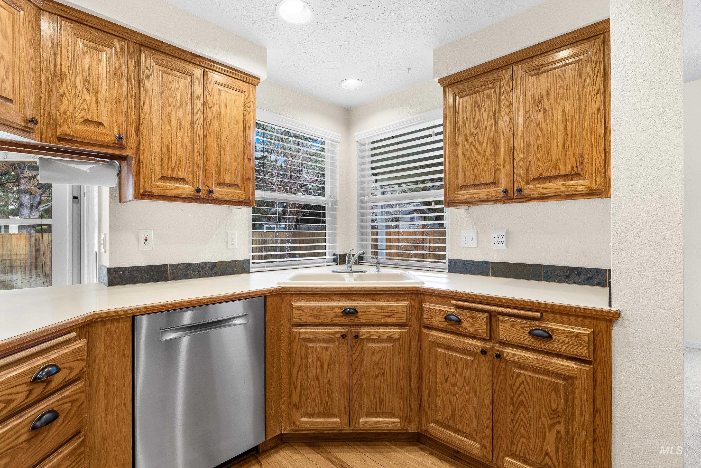 7736 West Bayhill Street Boise, ID 83704 - Photo 16 of 50 Kitchen with dishwasher, brown cabinetry, light countertops, a textured ceiling, and light wood-style flooring