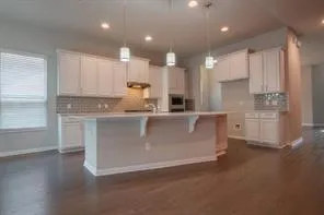 a large kitchen with stainless steel appliances granite countertop a stove a sink a refrigerator and white cabinets with wooden floor