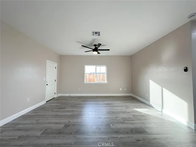an empty room with wooden floor ceiling fan and windows