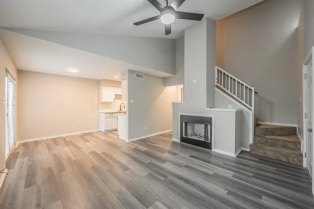 a view of an empty room with wooden floor and a kitchen