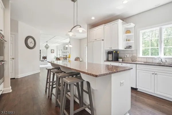 a open kitchen with granite countertop a stove a sink a dining table and chairs with wooden floor