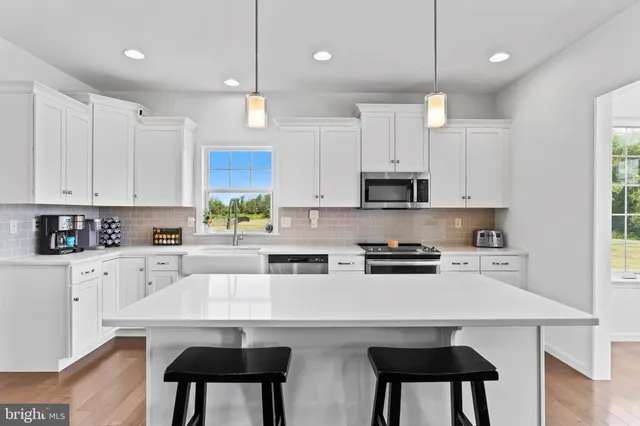 a kitchen with stainless steel appliances a stove a sink a refrigerator and white cabinets with wooden floor