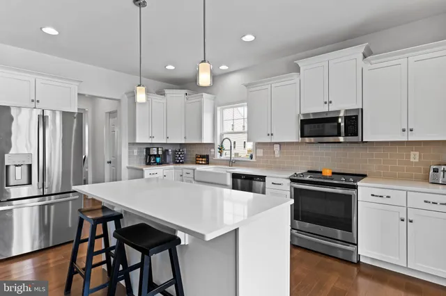 a kitchen with granite countertop a refrigerator a stove a sink and white cabinets with wooden floor