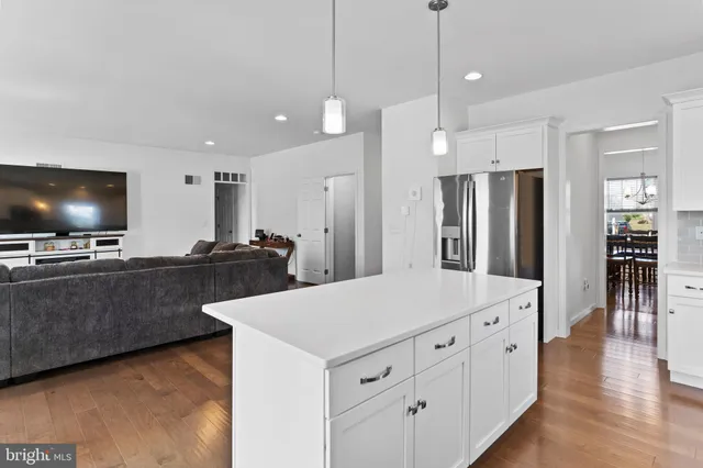 a kitchen with stainless steel appliances kitchen island granite countertop a refrigerator a oven a sink and white cabinets with wooden floor